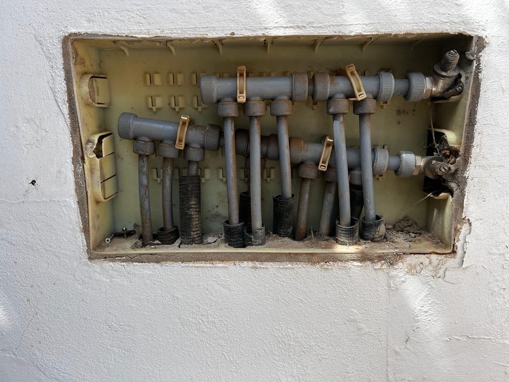 Old worn manifold in wall cavity showing corrosion and deterioration